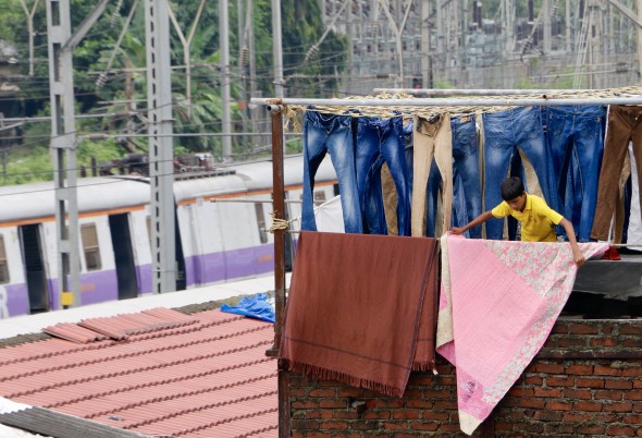 A young boy hangs sheets in Dhobi Ghat as a crowded train goes by.