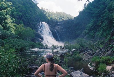 Woman standing in front of a waterfall in Far North Queensland, surrounded by rocks and shrubbery. 